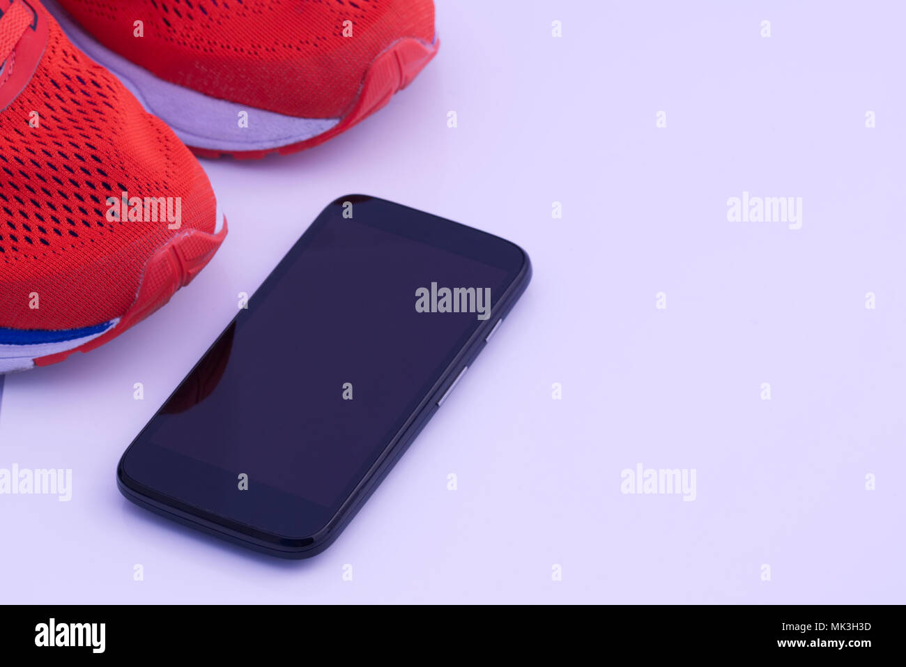 Vibrant orange running training shoes with black mobile phone cellphone isolated on a white background. Run, running concept Stock Photo