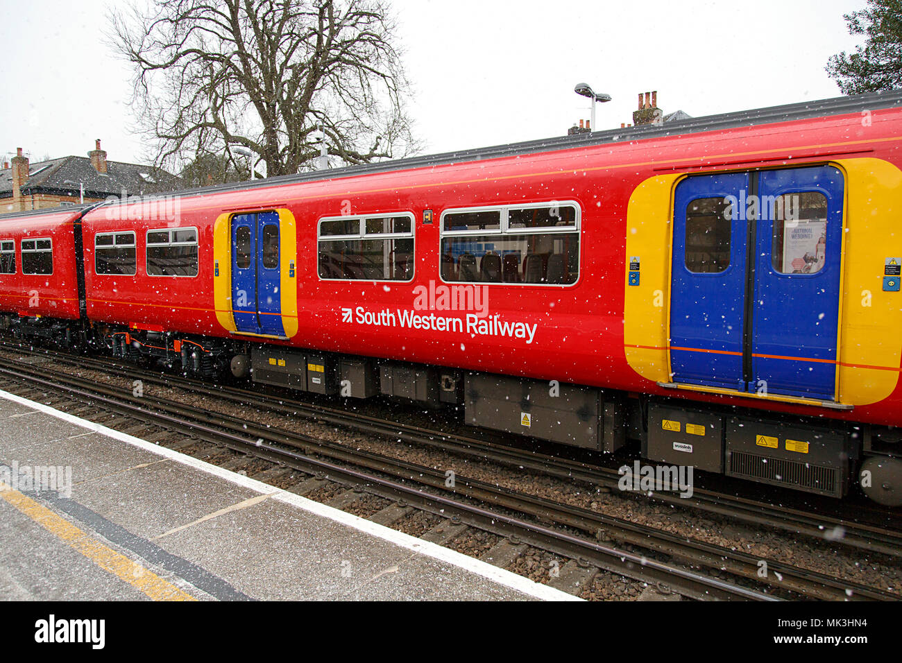 London, UK: February 26, 2018: A South Western Train pulls into Teddington Railway Station with snow falling causing a possible disruption to travel. Stock Photo
