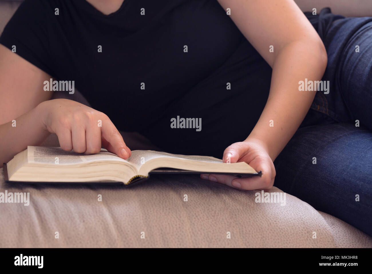 Young woman relaxing on the couch reading the Bible Stock Photo