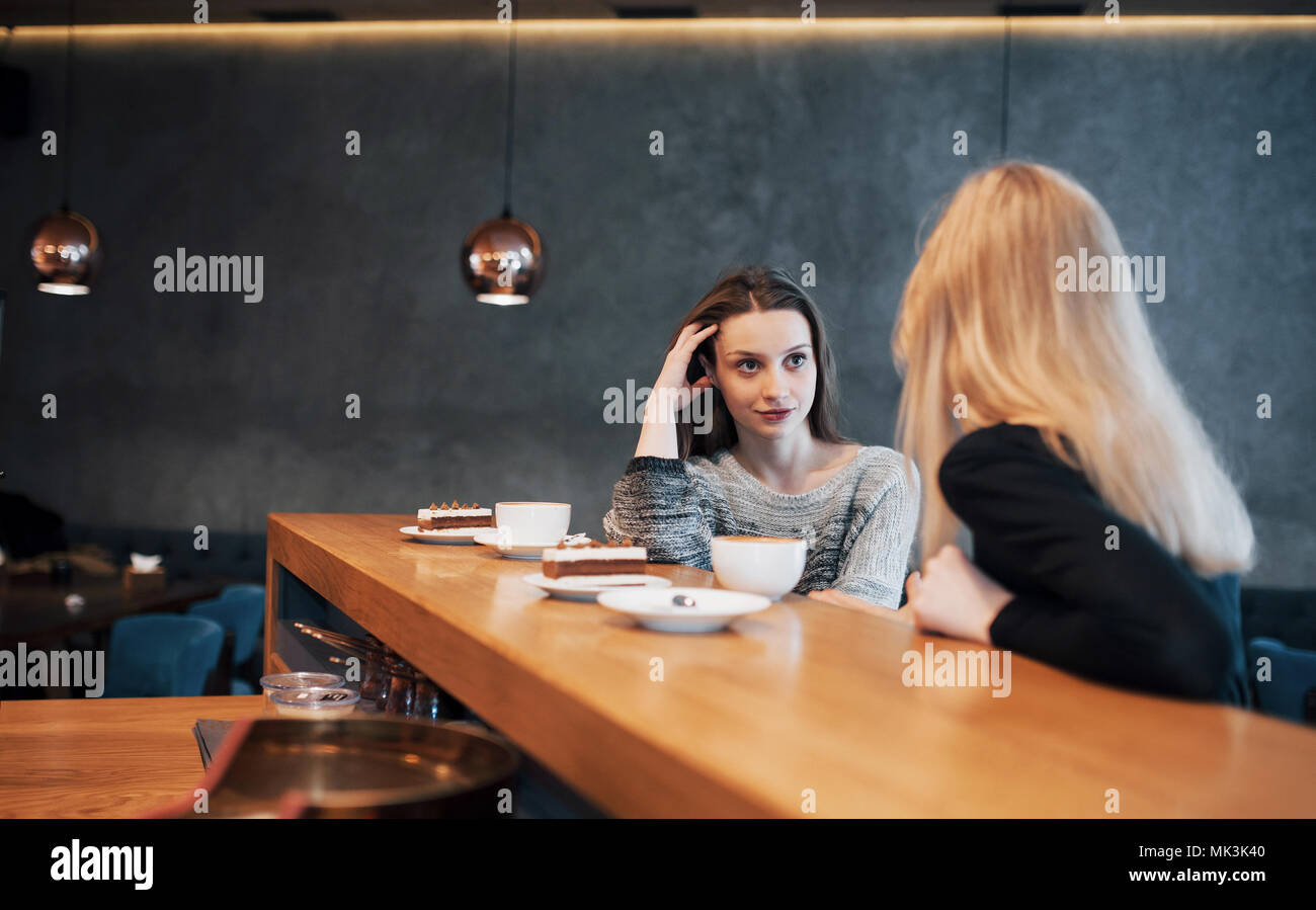 Two friends enjoying coffee together in a coffee shop as they sit at a table chatting Stock Photo