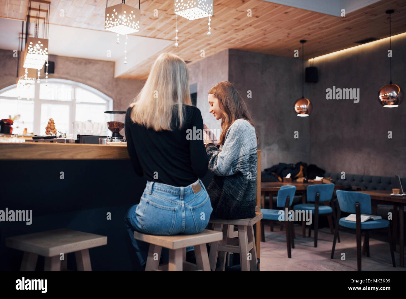 Two smiling friends reading funny online chat on modern telephone sitting with tasty coffee in restaurant.Hipster girls enjoying recreation time in cafe with hot beverages and messaging on cellular Stock Photo