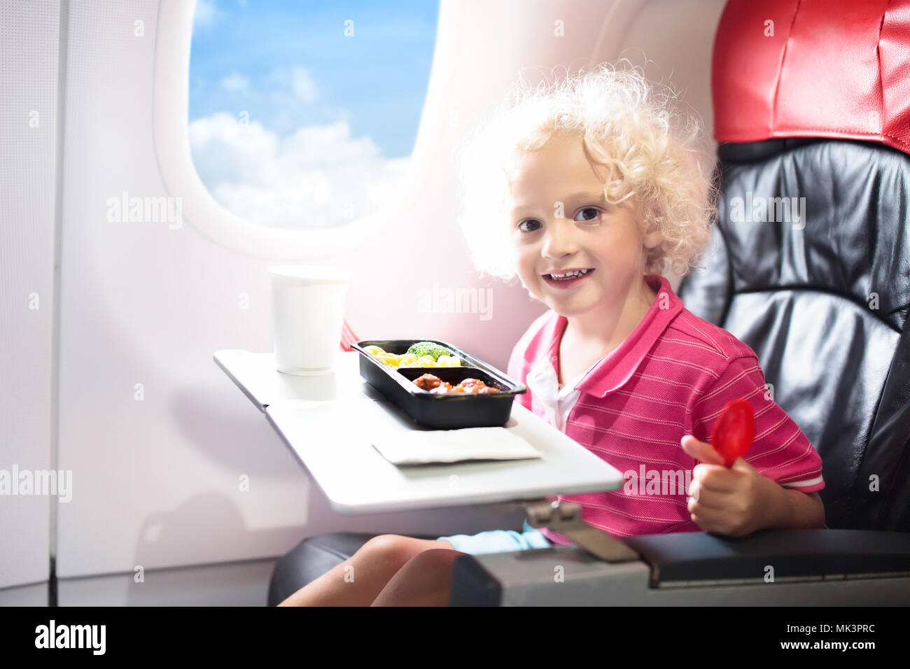 Child in airplane window seat. Kids flight meal. Children fly. Special inflight menu, food and drink for baby and kid. Little boy eating healthy lunch Stock Photo
