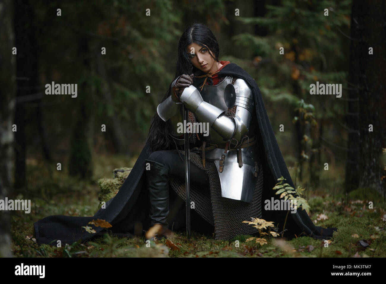 A beautiful warrior girl with a sword wearing chainmail and armor in a mysterious forest Stock Photo
