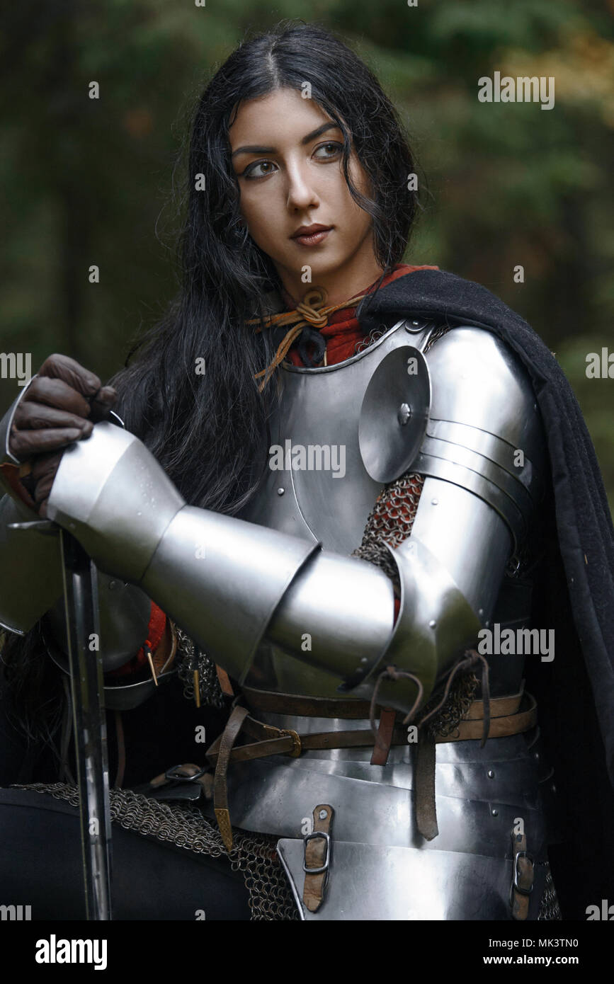 A beautiful warrior girl with a sword wearing chainmail and armor in a mysterious forest Stock Photo