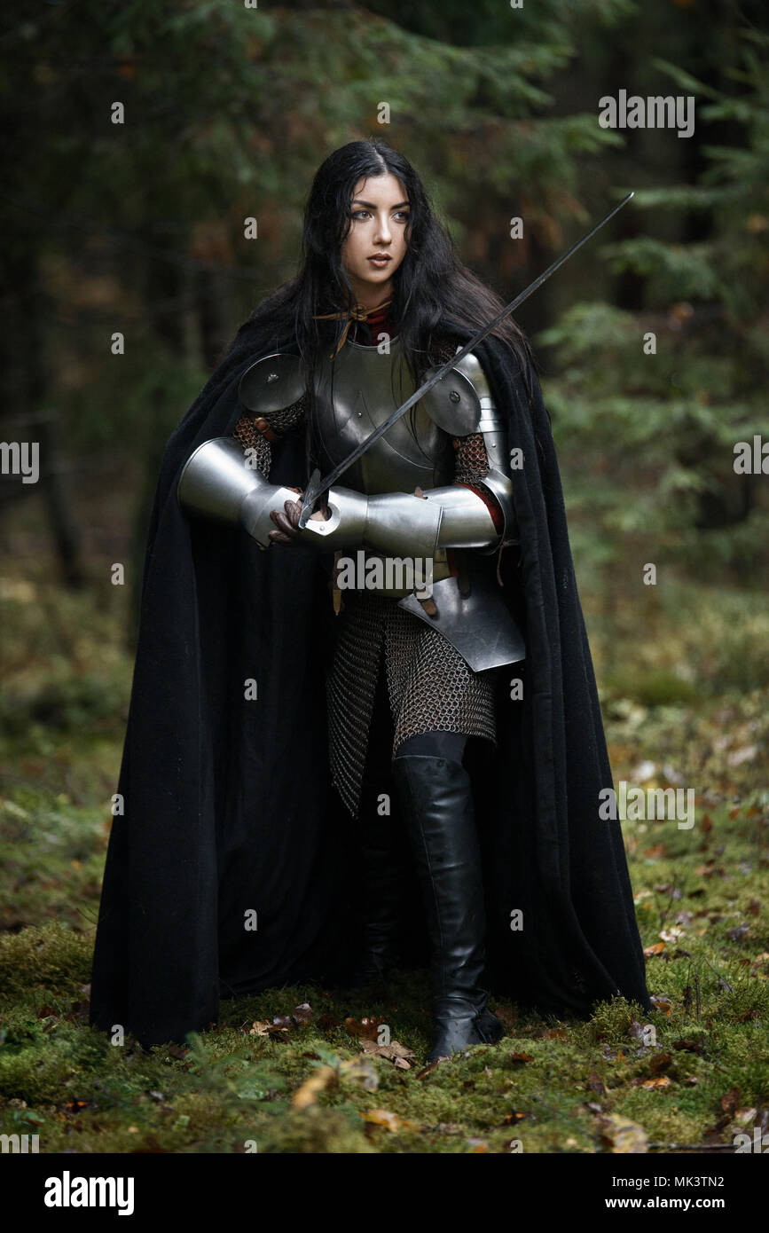 A beautiful warrior girl with a sword wearing chainmail and armor in a mysterious forest Stock Photo