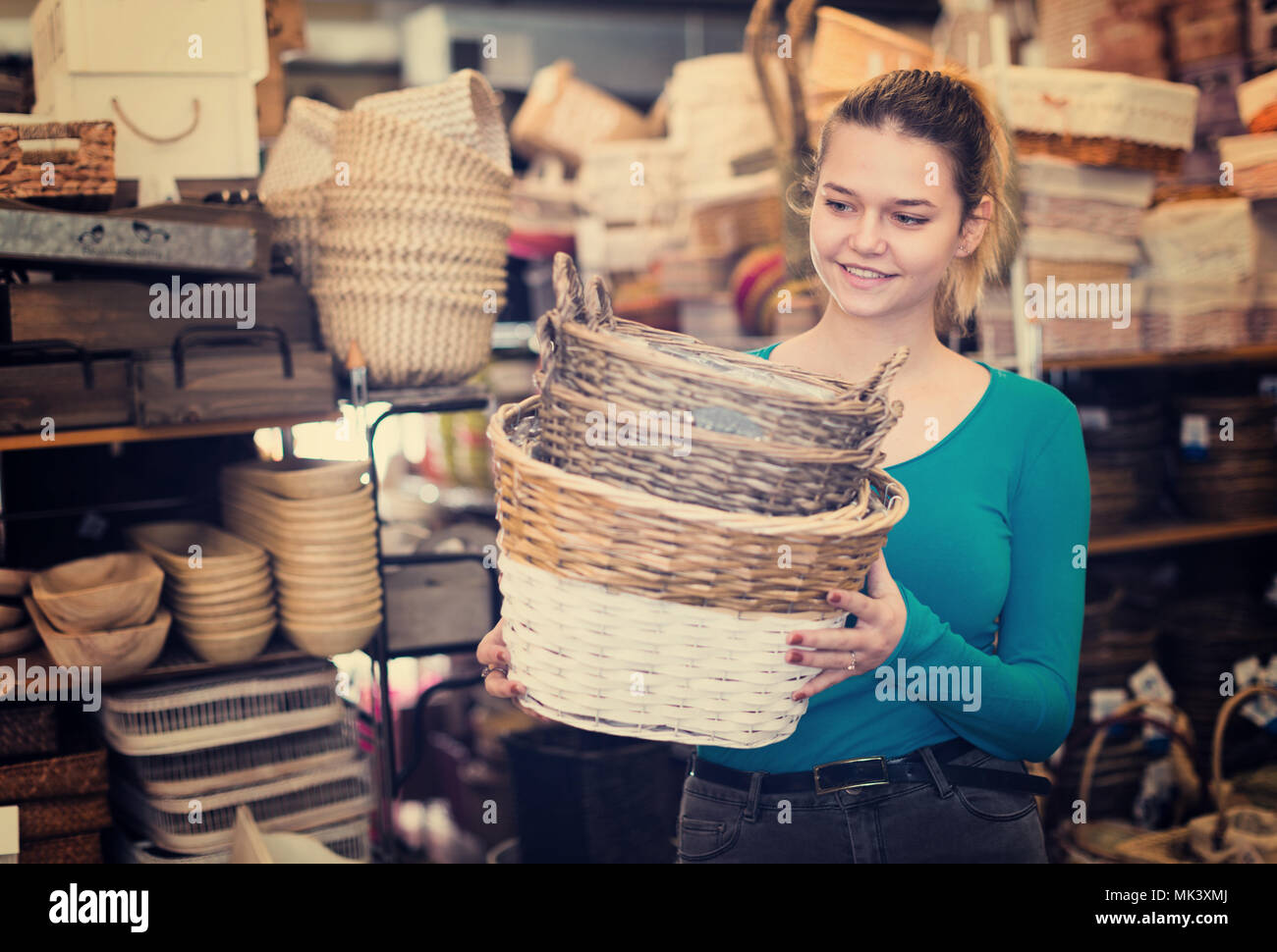 Smiling young woman consumer holding wicker basket in decor items store ...