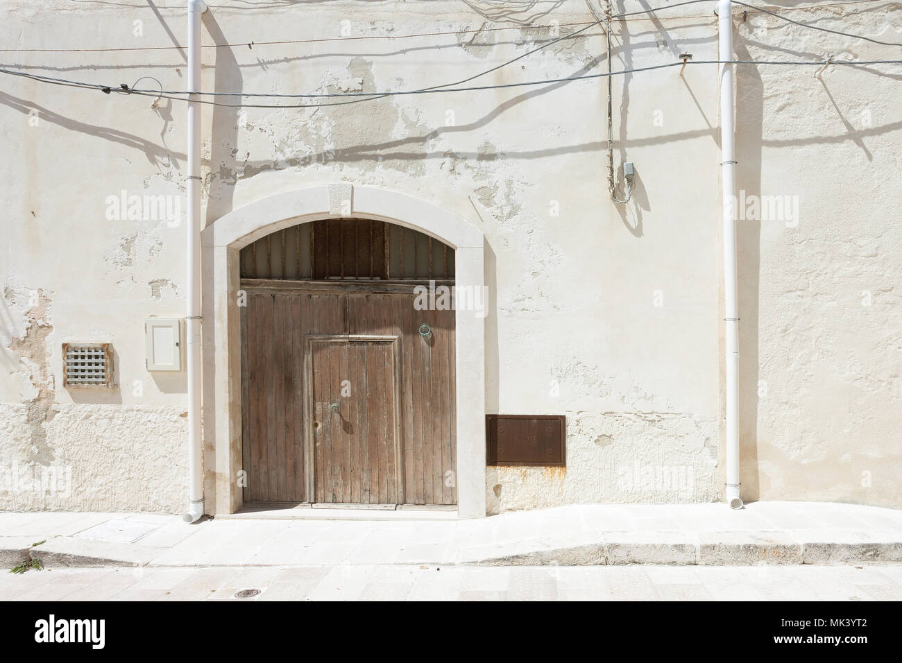 Vieste, Apulia, Italy - A folding gate, two rainwater pipes and some cables Stock Photo