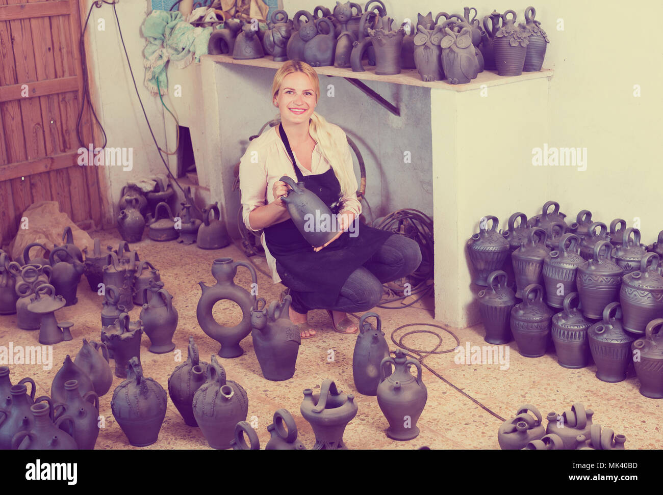 portrait of cheerful female artisan with black-glazed ceramic vases in atelier Stock Photo