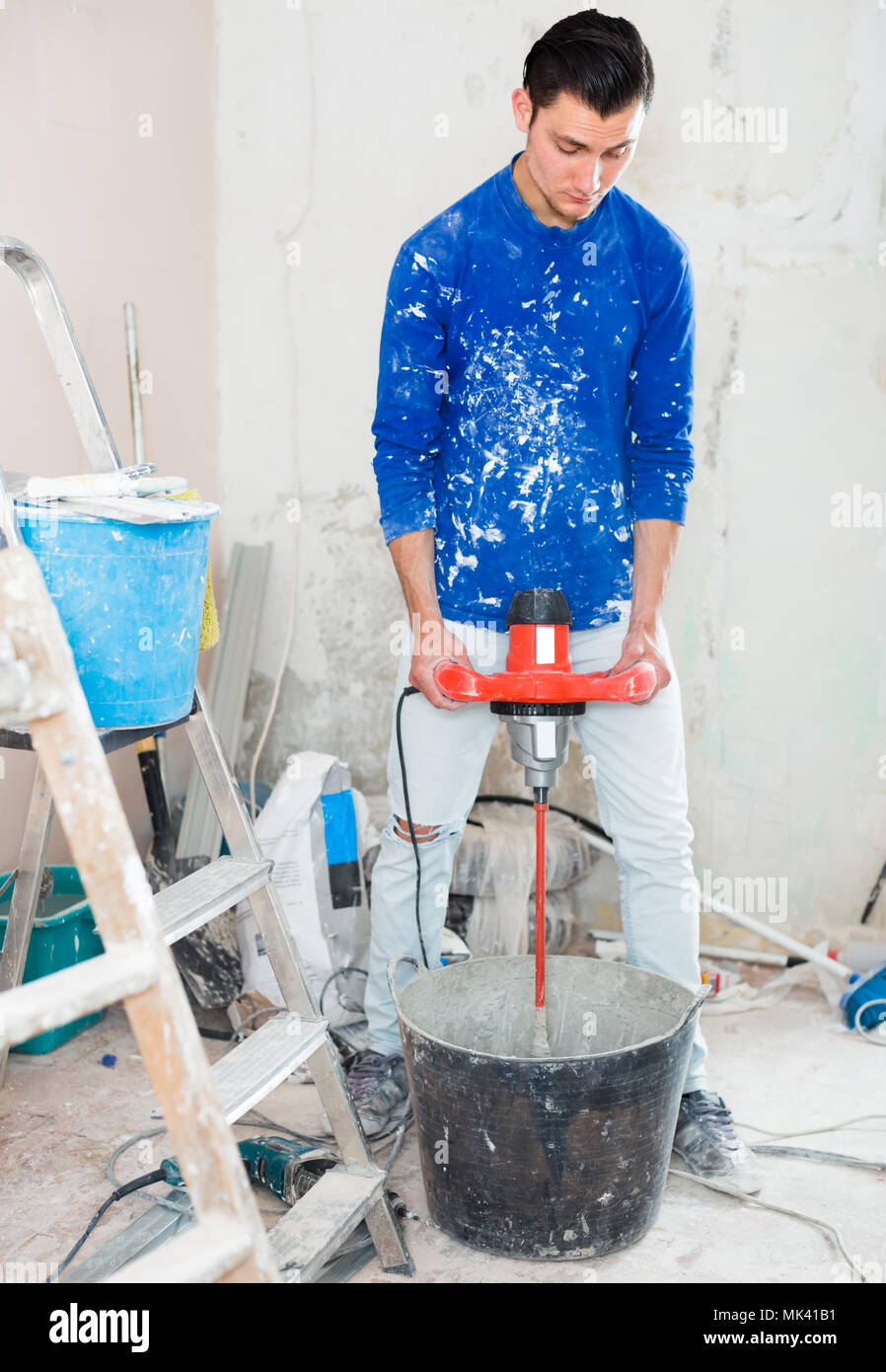 builder mixing plaster in bucket using electric mixer in repairable room Stock Photo