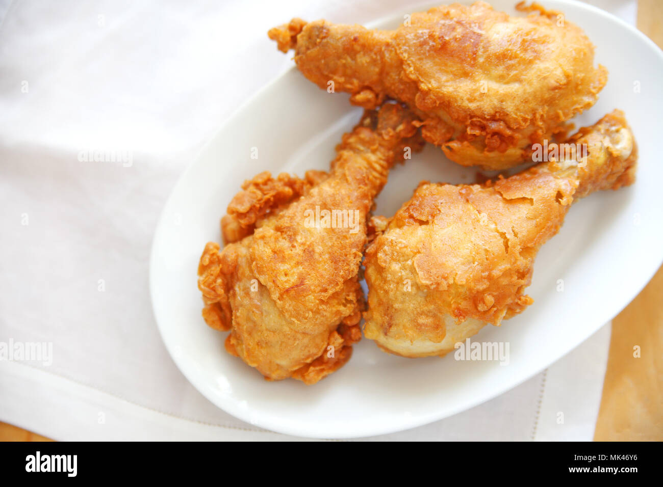 Three fried chicken legs on a white dish with a white napkin and copy