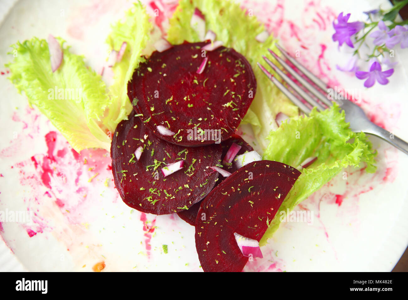Beet slices with red onion bits, lettuce and grated lime zest on a beet juice-stained plate Stock Photo