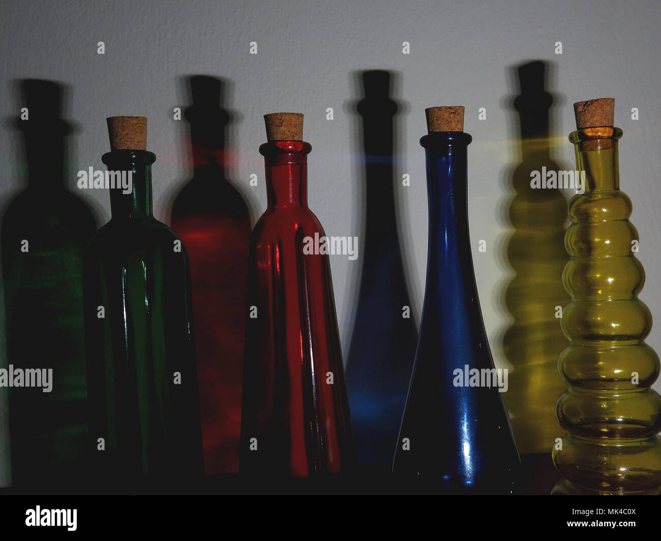 Illuminated coloured bottles casting shadows on wall. Stock Photo