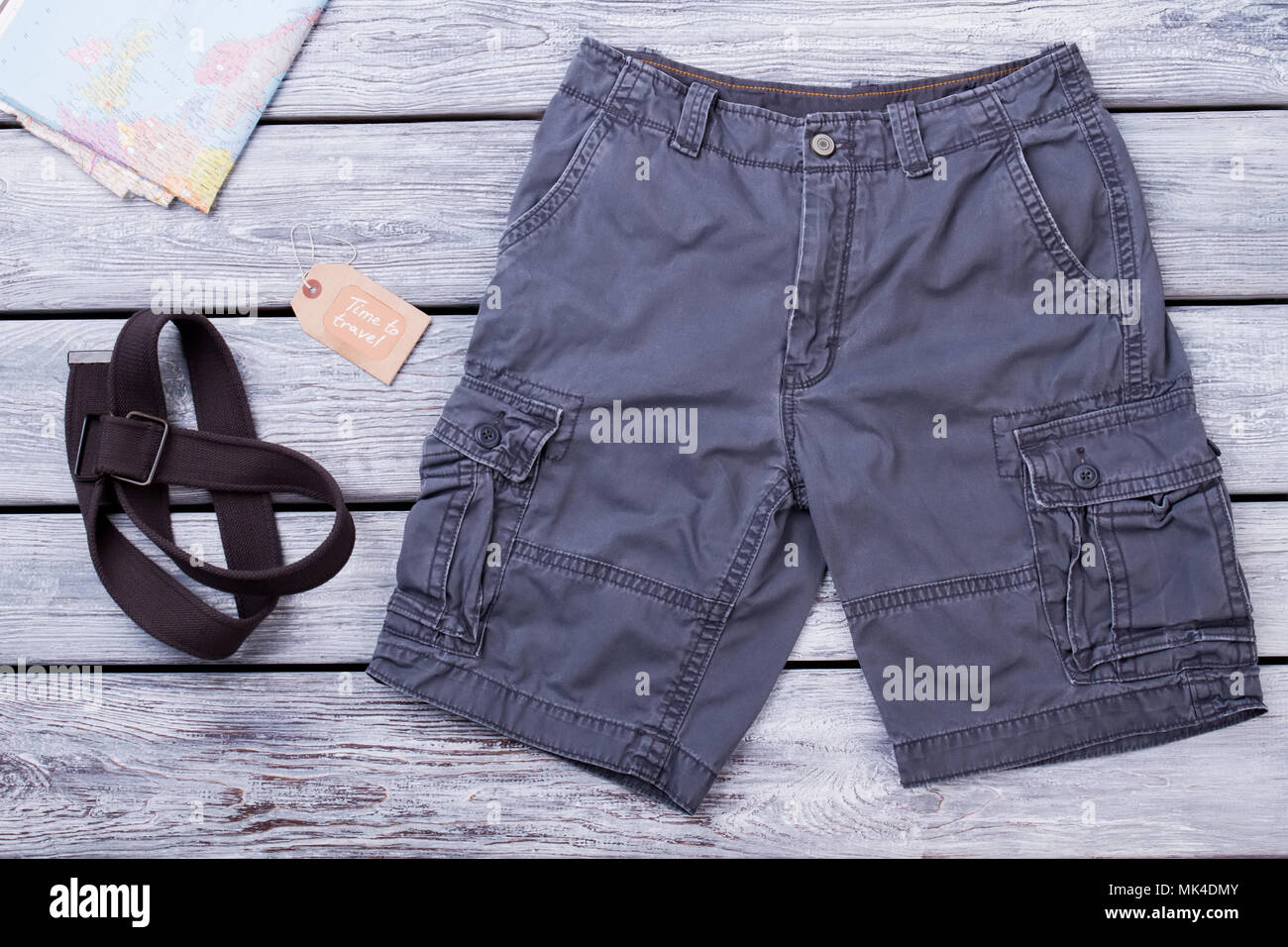 Travel clothes and equipment. Black shorts, map and strap. Wooden desk surface background. Stock Photo