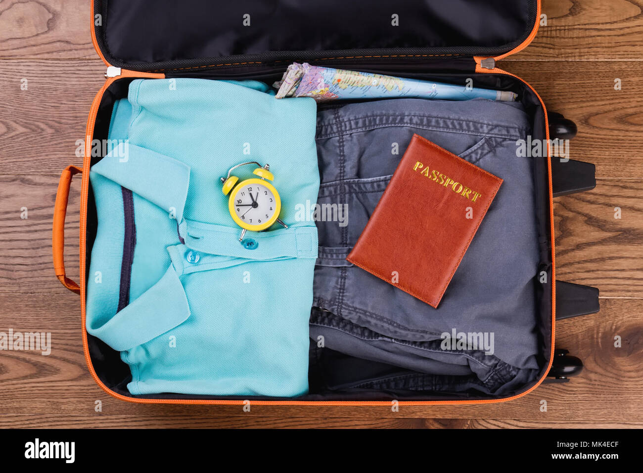 Packing suitcase for vacation top view. Flat lay. Male apparel, yellow alarm clock and passport. Stock Photo
