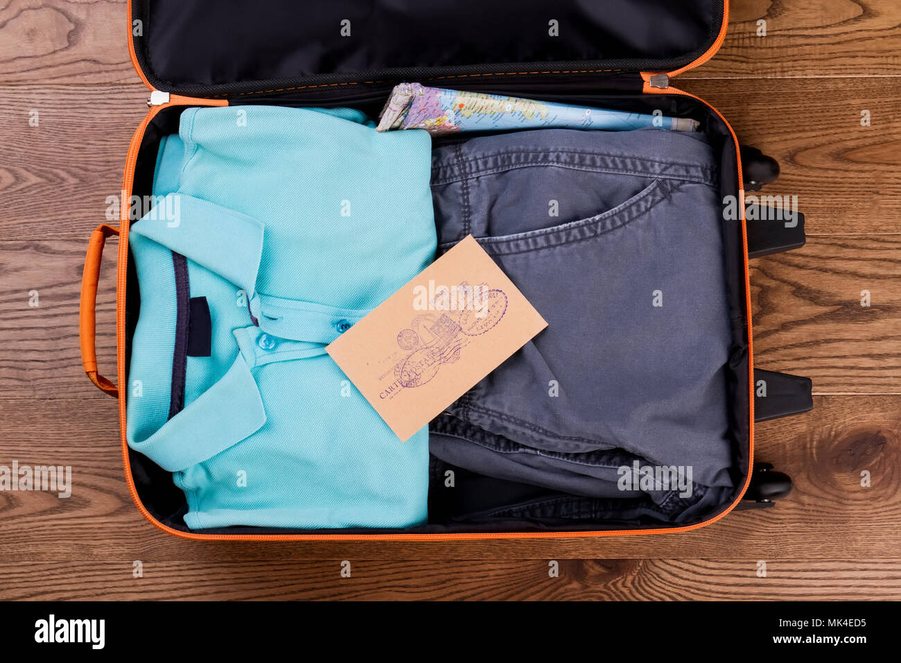 Suitcase packed with neatly folded clothes. Map and mail with stamps. Stock Photo
