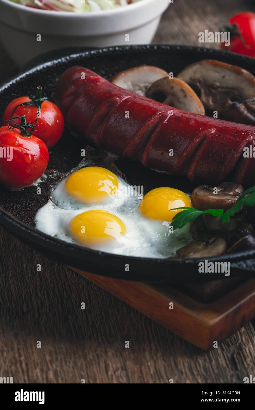 Fried quail eggs, sausage,  tomatoes and mushrooms on cast iron skillet, English breakfast rustic style Stock Photo
