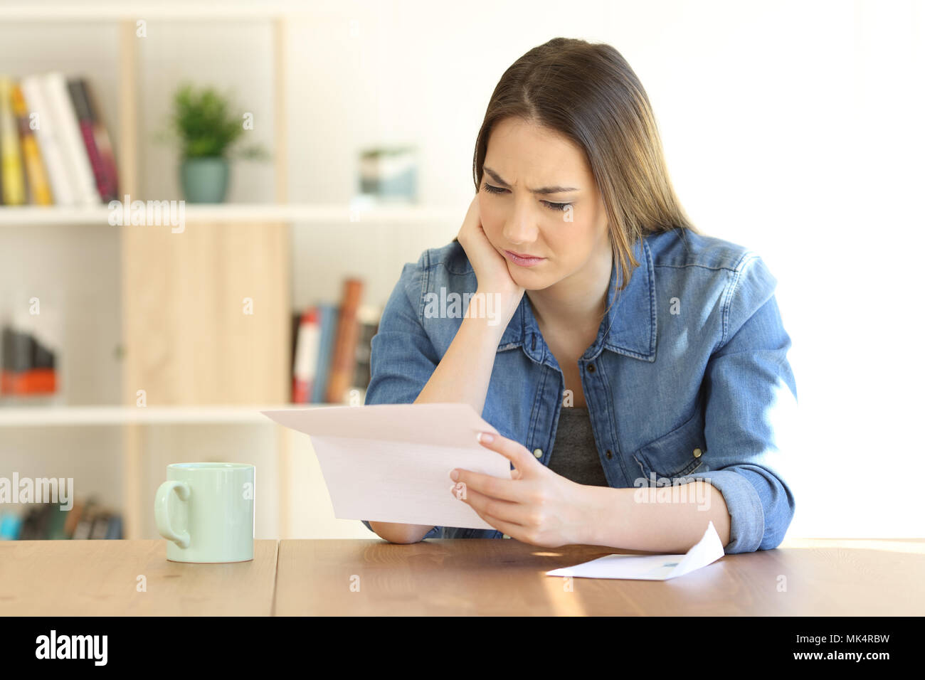 Portrait of a worried female reading a paper letter on a table at home Stock Photo