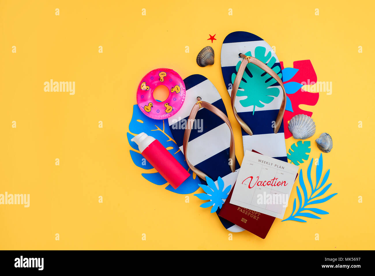 Summer holiday concept, travel and beach accessories with copy space. Flip flops, tropical leaves and a calendar with Vacation note on a vibrant yellow background. Stock Photo