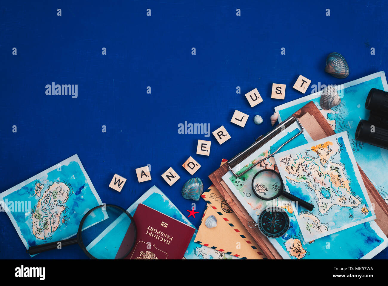 Header with travel and exploration concept. Watercolor maps, passport, compass, binoculars, envelopes, and Wanderlust scrabble letters flat lay on a navy blue background with copy space Stock Photo