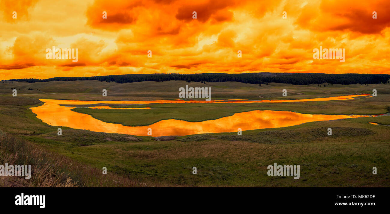 Sunset on the river in wide open fields. The river reflecting the color of the sky. Panoramic. Stock Photo
