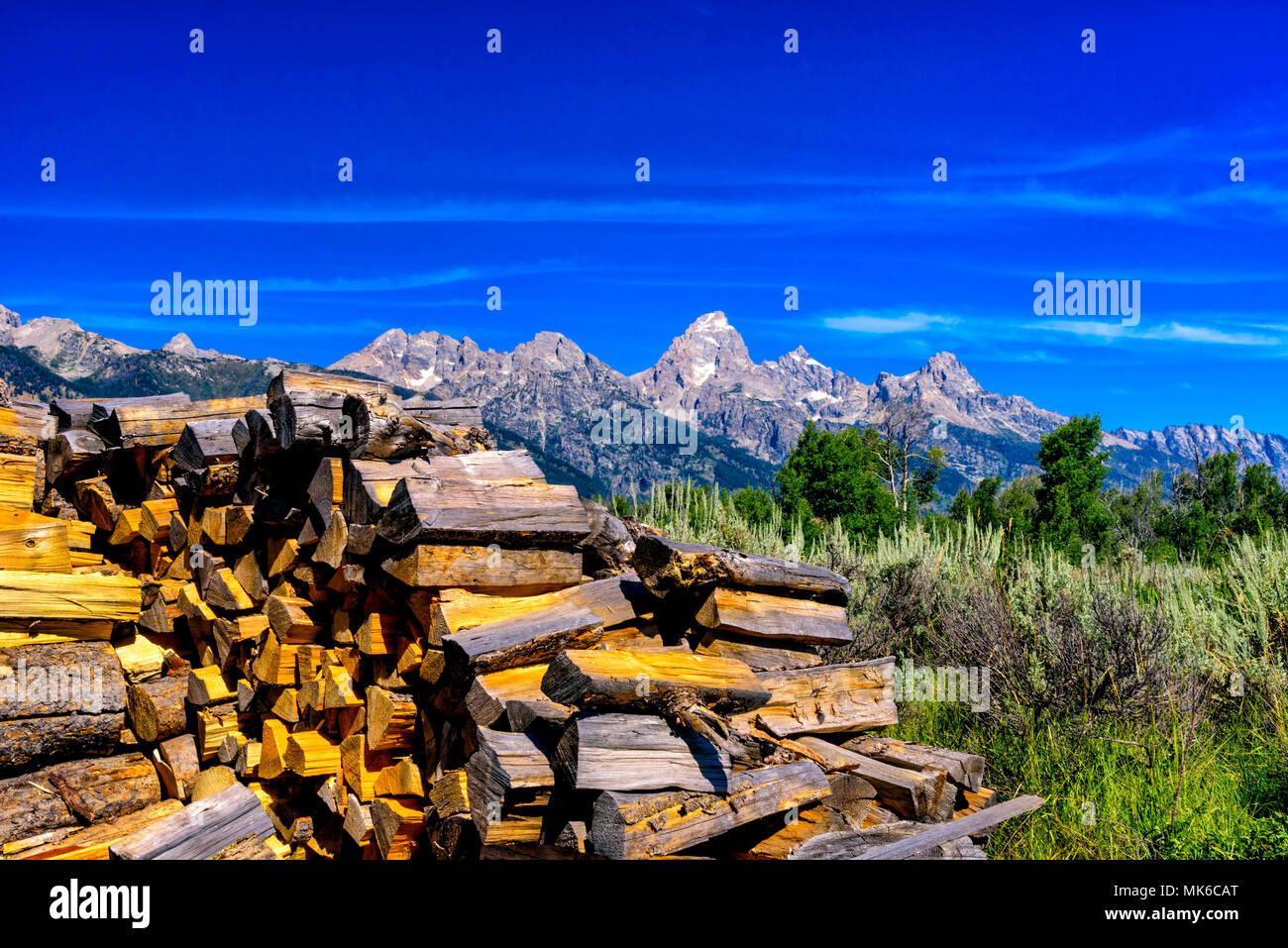 Winter wood pile near field with Teton mountains in back ground under blue sky. Stock Photo