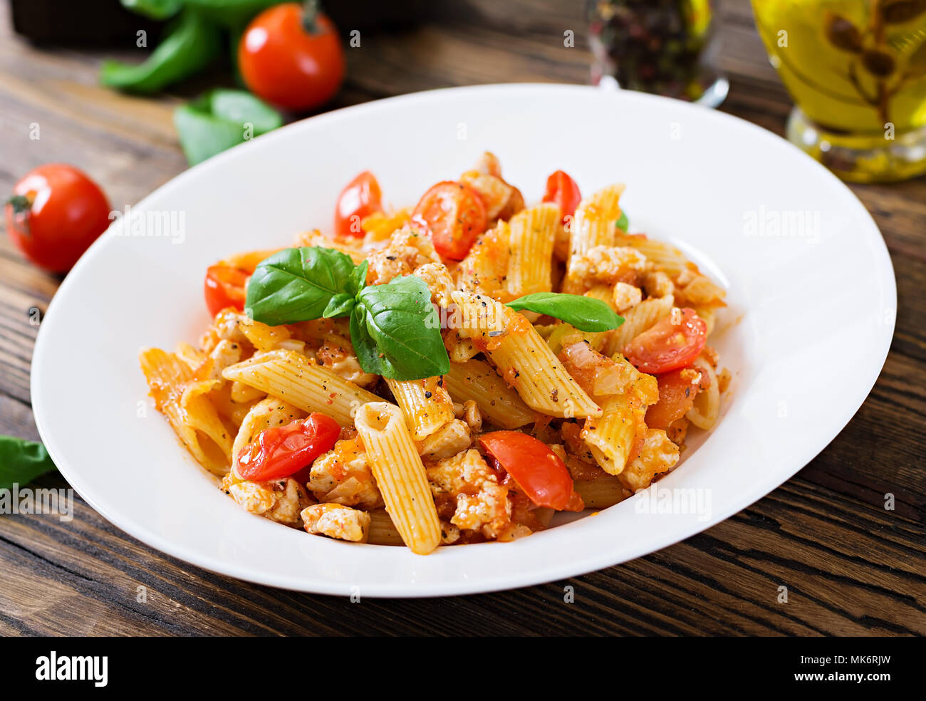Penne pasta in tomato sauce with chicken, tomatoes, decorated with basil on a wooden table. Italian food. Pasta Bolognese. Stock Photo