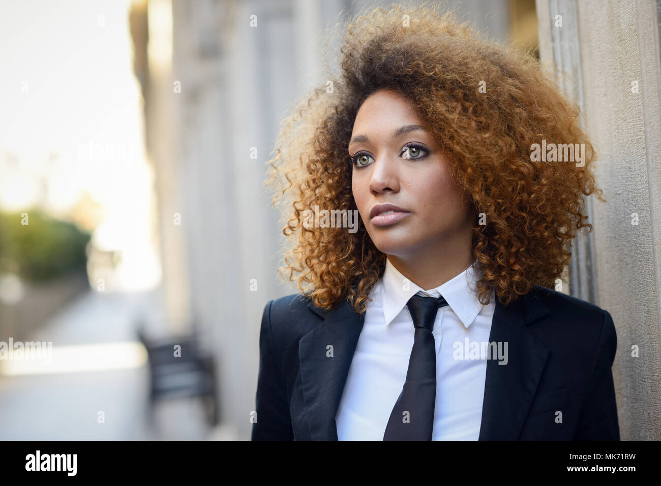 Portrait of beautiful black businesswoman wearing suit and tie in urban ...