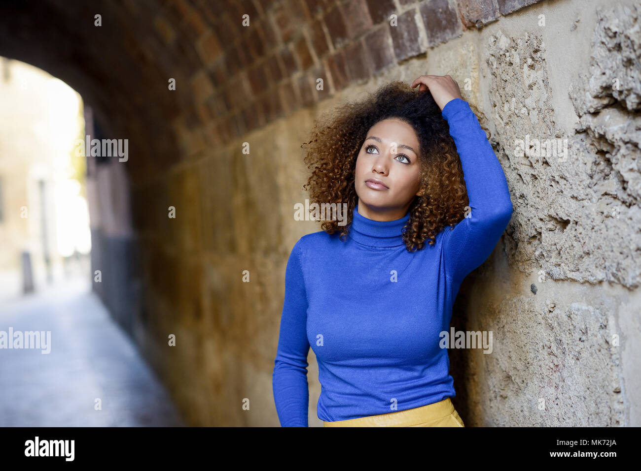 Beautiful young African American woman, model of fashion, with afro hairstyle and green eyes wearing blue sweater in urban background Stock Photo