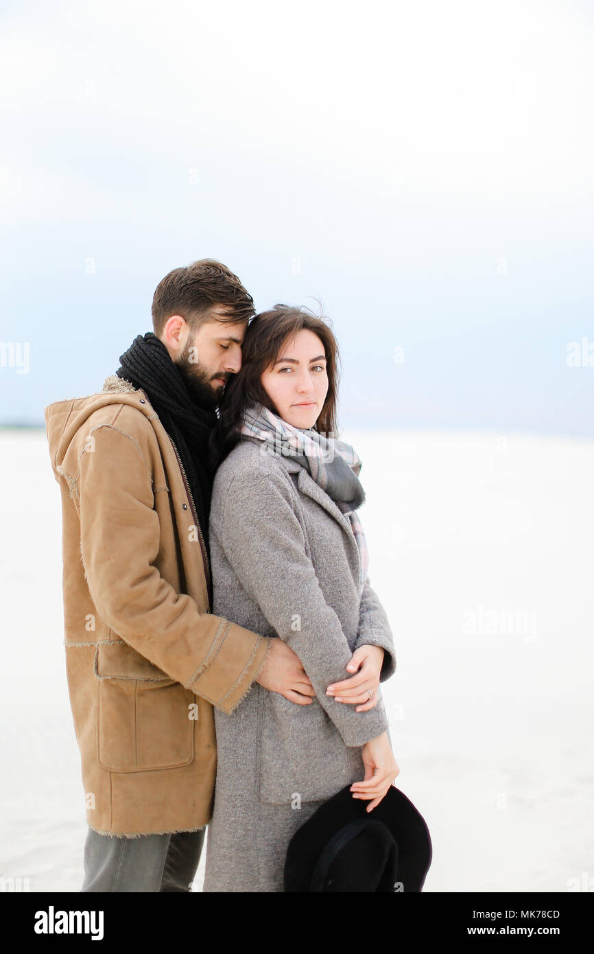 Young man hugging pretty woman wearing grey coat and scarf in white ...