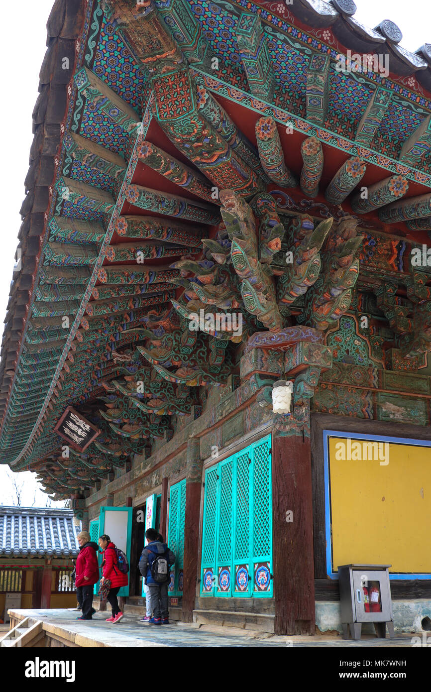 Three visitors emerge from the Geuknakjeon Hall at Bulguksa Temple in South Korea.The complex roof eaves have intricate multicolored painted patterns. Stock Photo