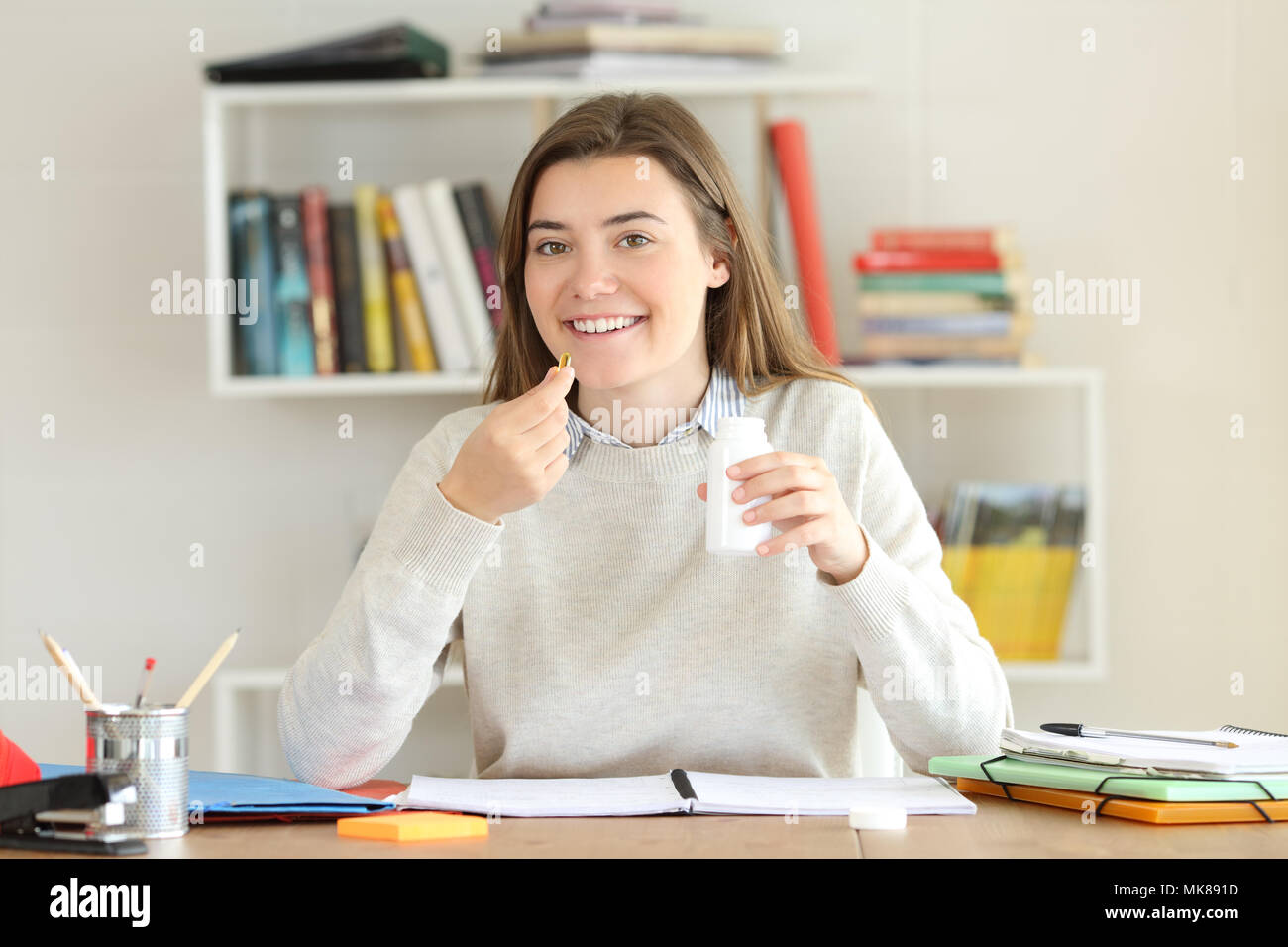 Front view portrait of a happy student holding vitamin supplement pills at home Stock Photo