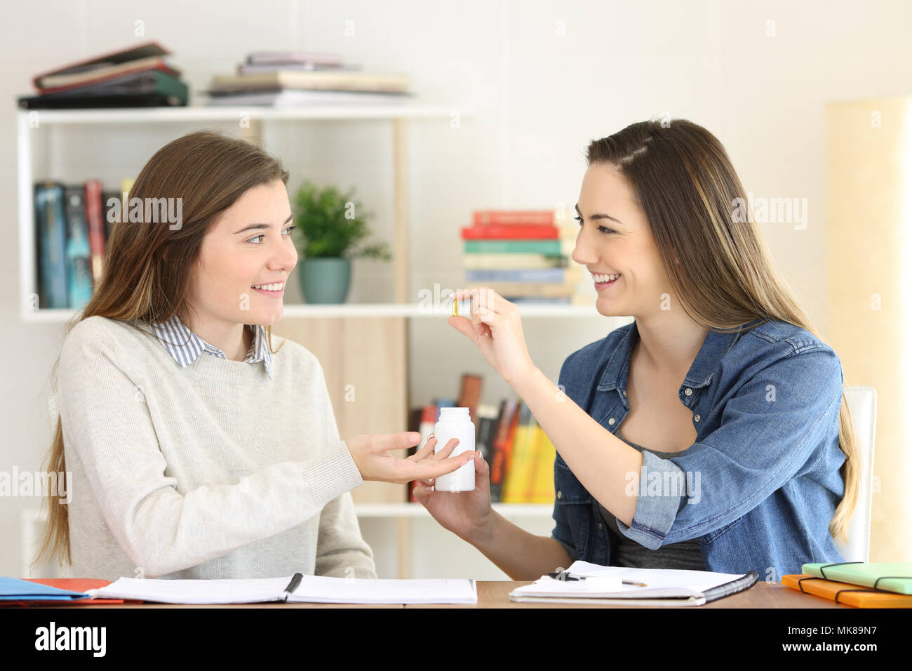Student studying and offering a vitamin supplement to a friend at home Stock Photo