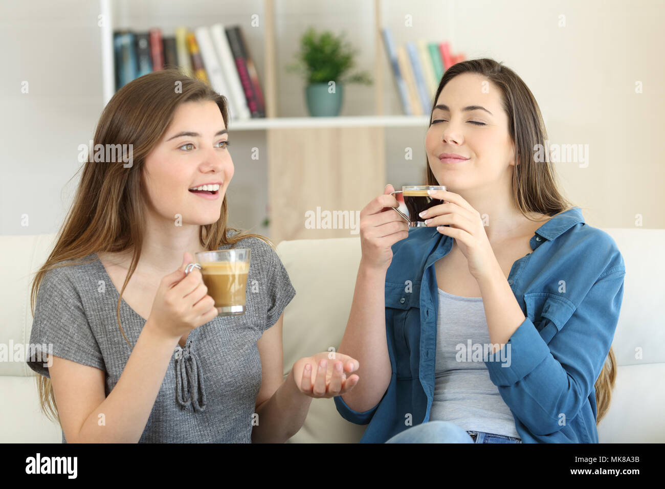 Two friends talking and enjoying a coffee cup sitting on a couch in the living room at home Stock Photo