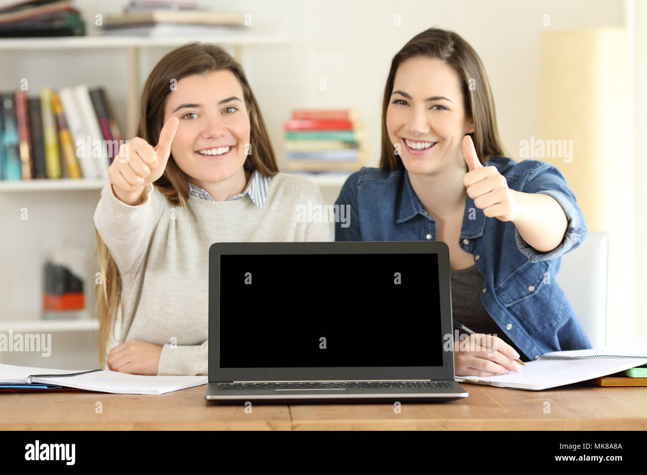 Front, view portrait of two happy students showing a blank laptop screen mockup on a desktop at home Stock Photo