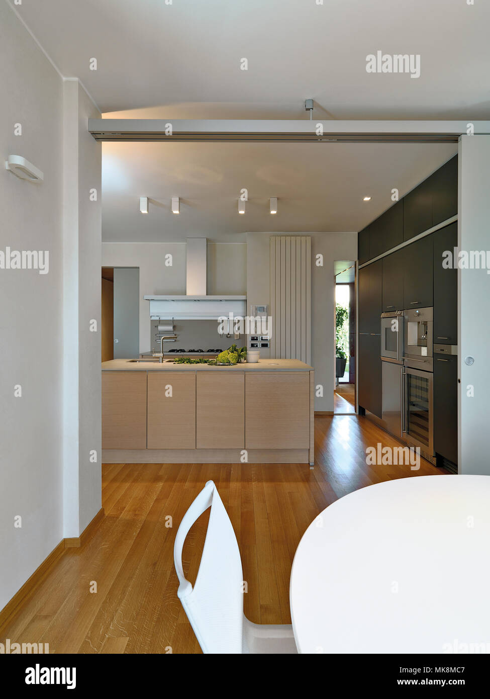 interiors shots of a modern kitchen with kitchen isanad in the foreground the white dining table the floor is made of wood Stock Photo
