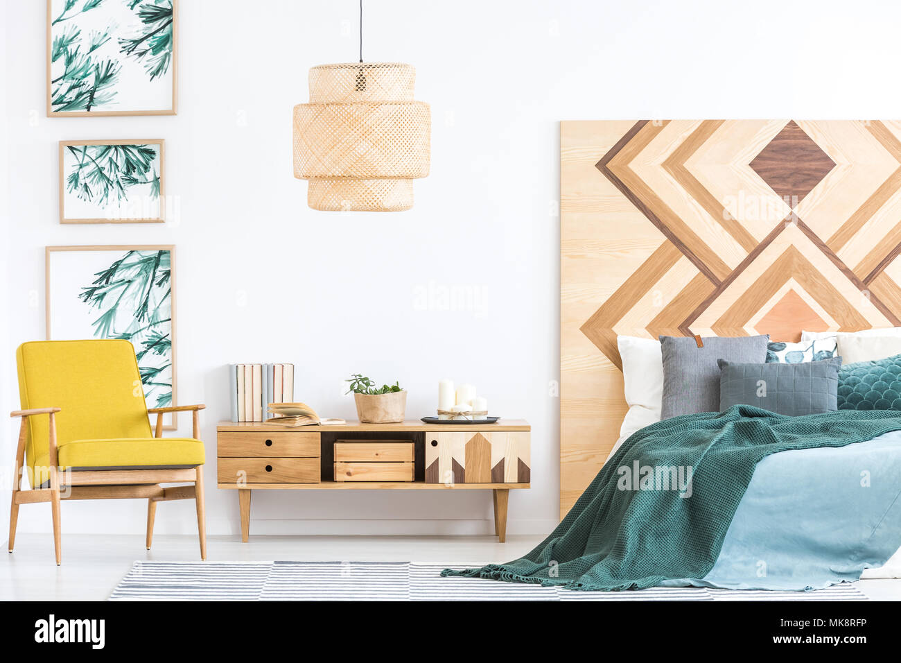 Wooden cupboard between yellow armchair and green bed in bedroom