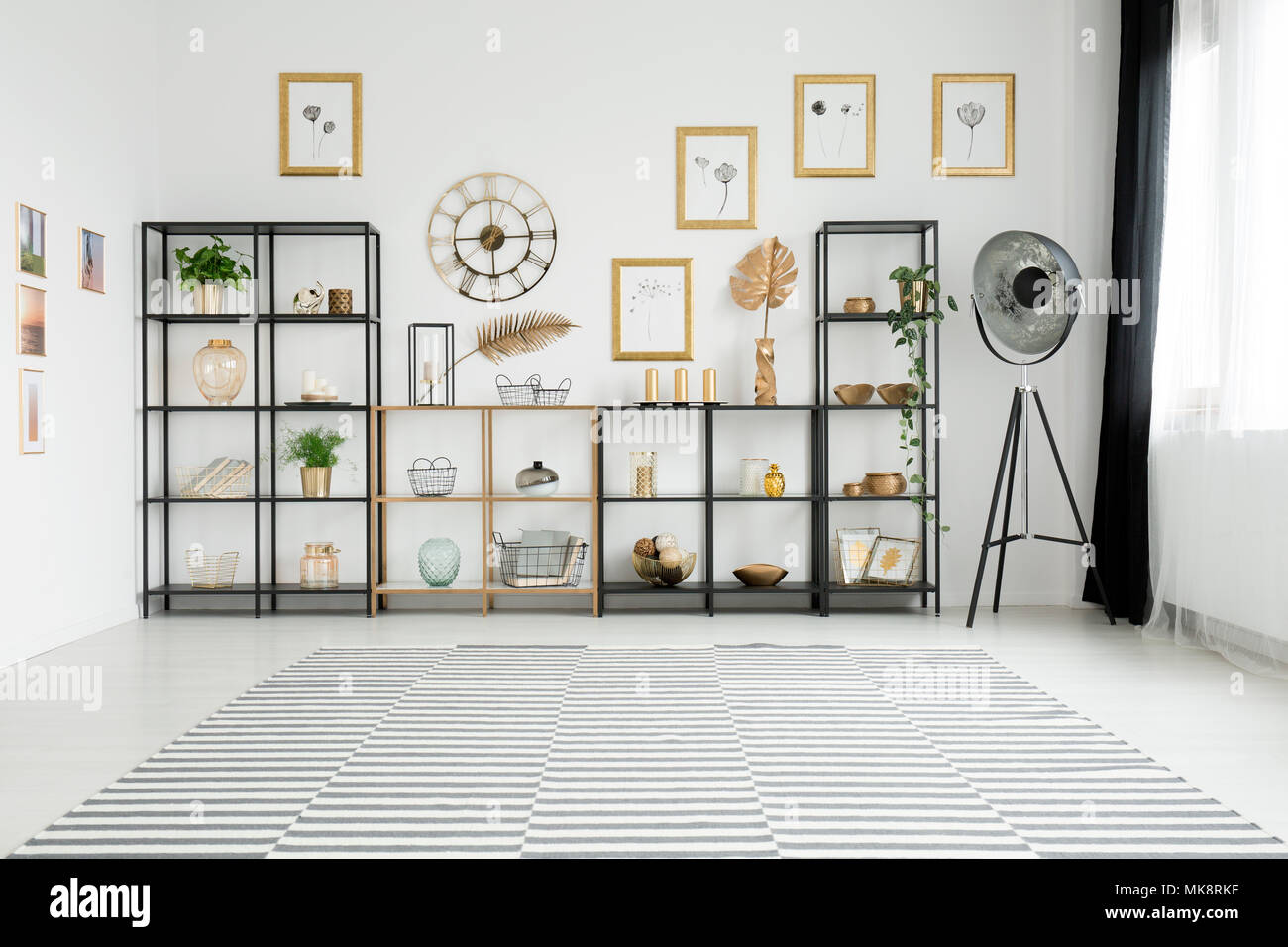 Spacious living room interior with lots of decorations on gold and black racks standing against a white wall with pictures gallery Stock Photo