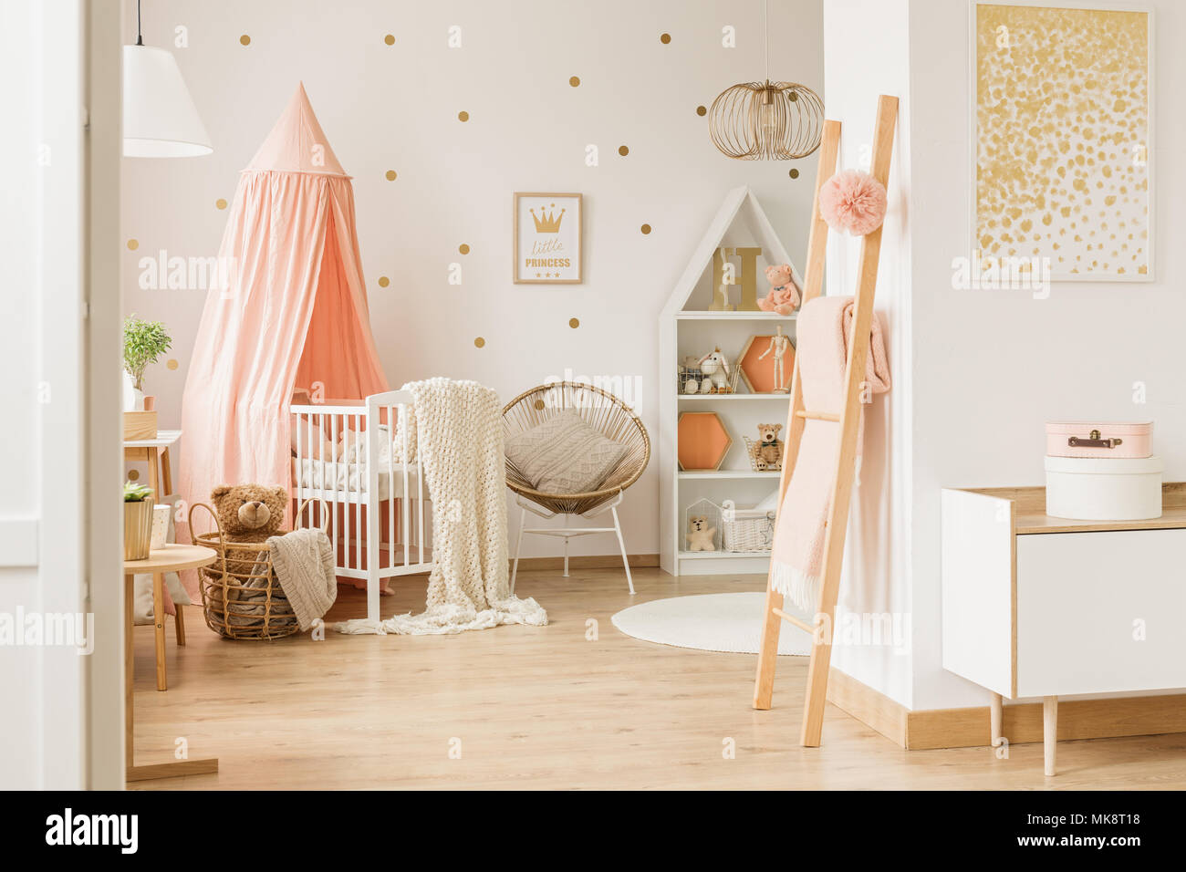 Wooden ladder with dirty pink blanket and pompom in bright baby room interior with gold decor and canopy crib Stock Photo