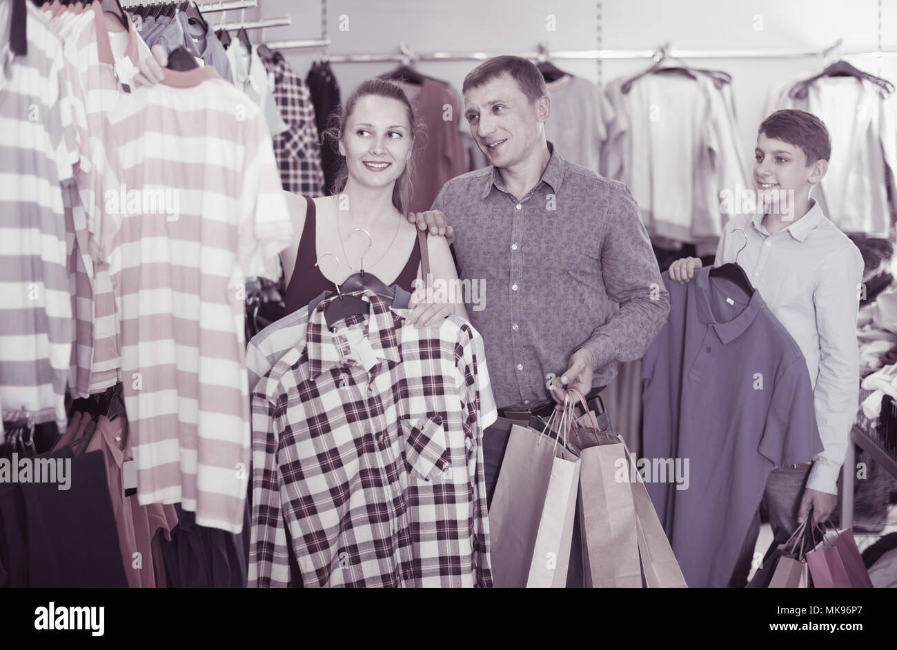 happy man, woman and boy stands near clothes and choosing man shirt in ...