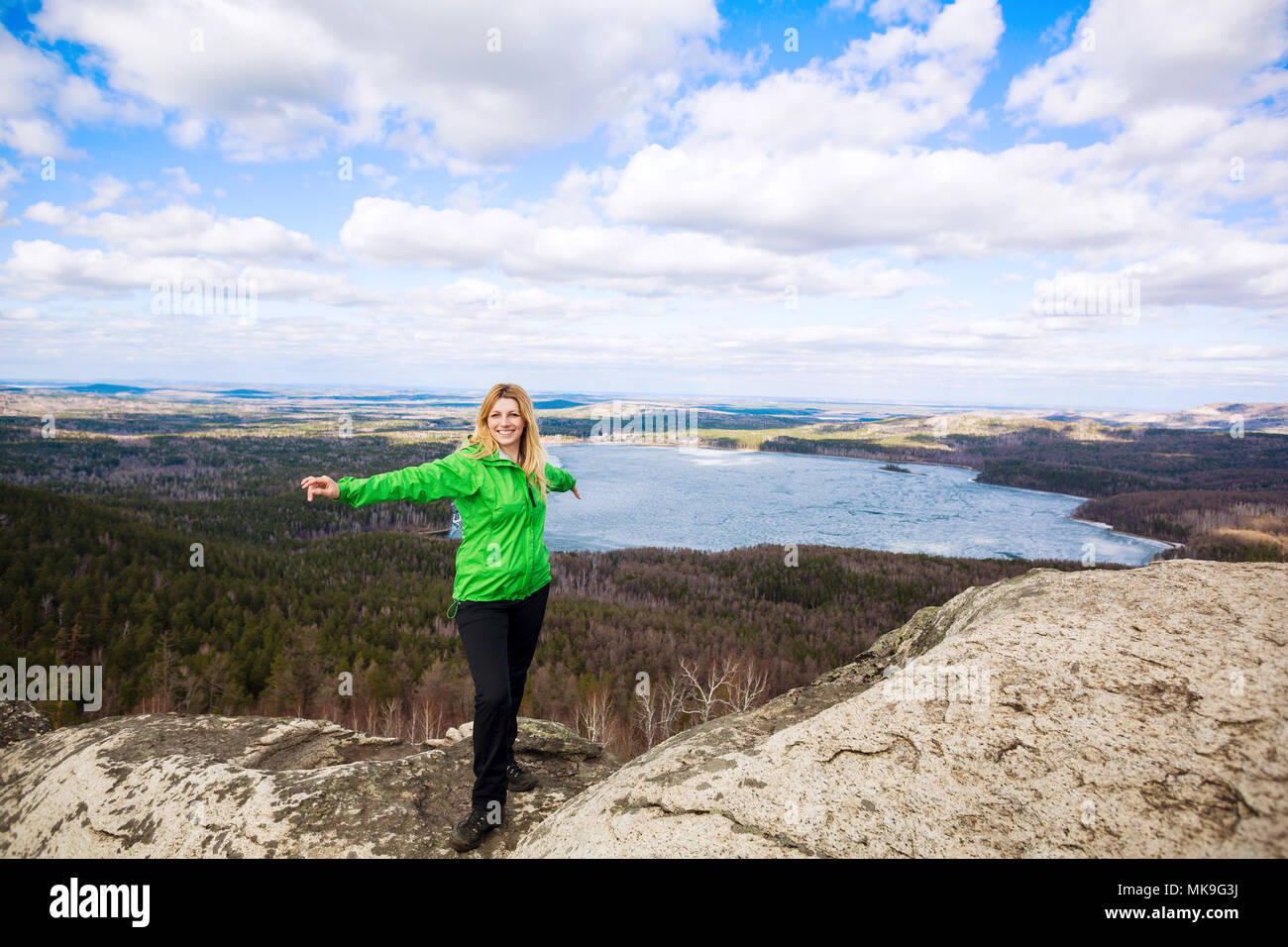 Young woman standing on cliff edge with raised hands Stock Photo