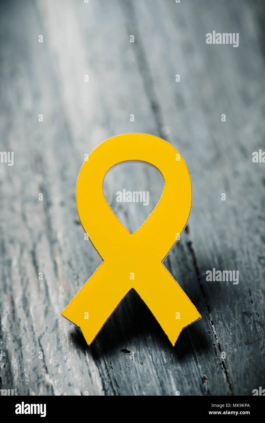 closeup of a yellow ribbon on a gray rustic wooden surface, with some blank space on top Stock Photo