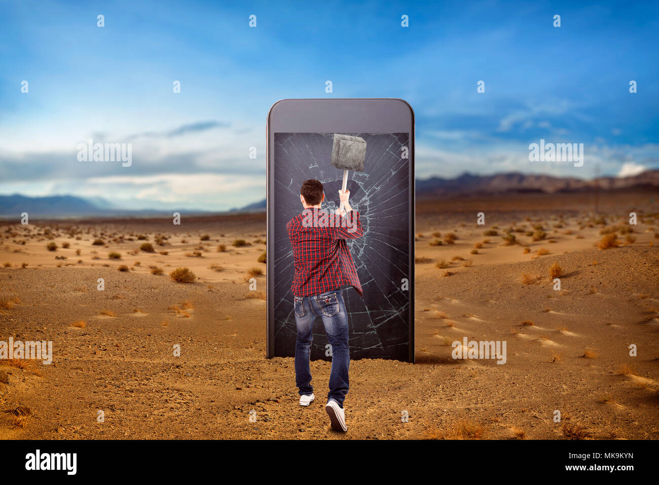 Phone addicted people, loneliness in the net concept. Man smashes a large smartphone screen with a sledgehammer, desert valley on background. Manipula Stock Photo
