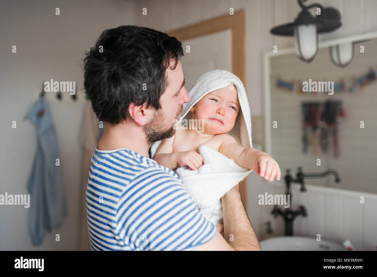 Father with a toddler child wrapped in towel in a bathroom at home. Stock Photo