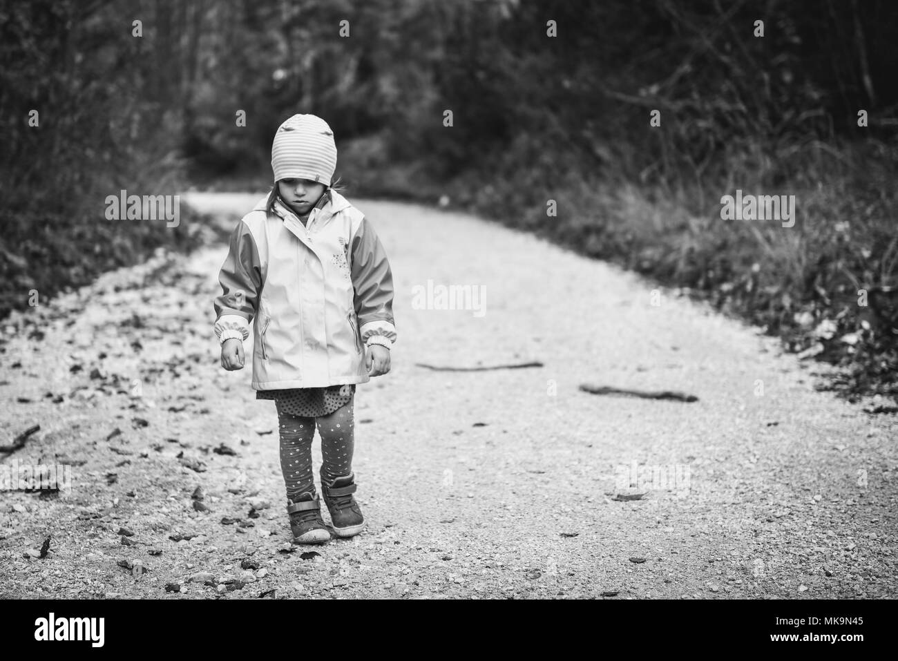 Young sad girl child is walking alone on country road. Abandoned sad little girl is walking in nature and looking down. Concept of loneliness, abandon Stock Photo
