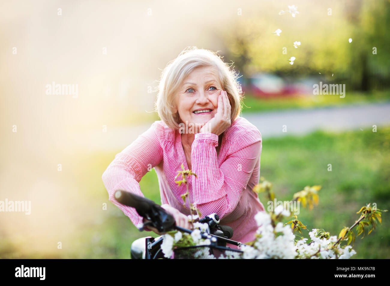 Beautiful senior woman with bicycle outside in spring nature. Stock Photo