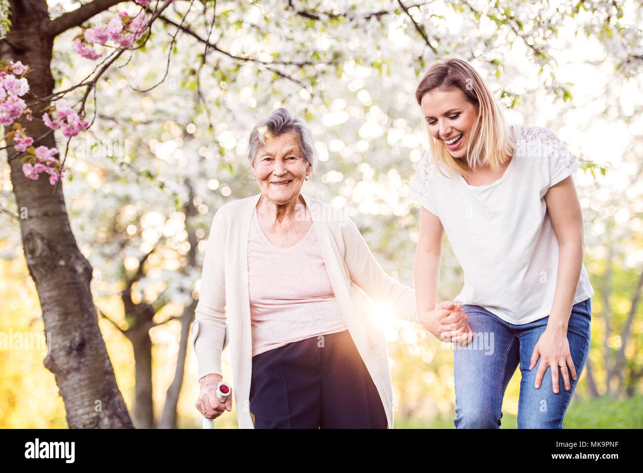 Elderly grandmother with crutch and granddaughter in spring nature. Stock Photo