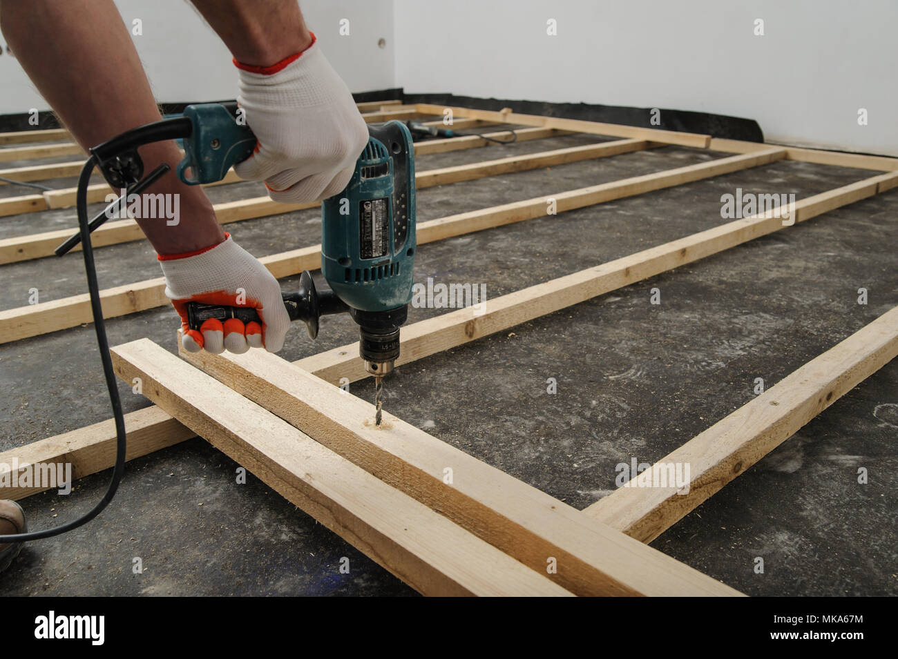 Worker drill holes in the wooden beams using an electric drill. Stock Photo