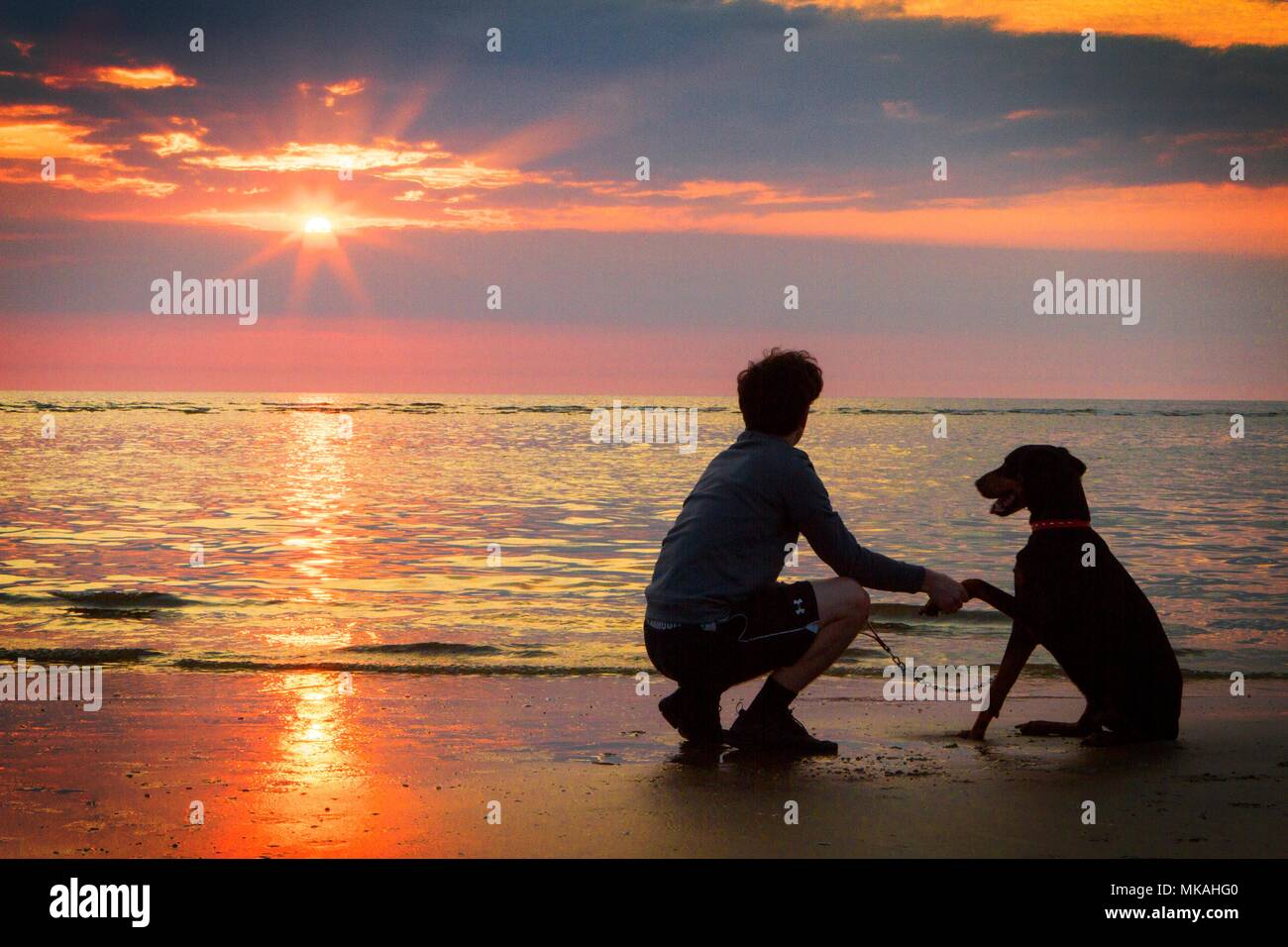 Southport, Merseyside. 7th May 2018. UK Weather.  Sam Elias [MR] stands with his best friend 'Charlie' the Doberman Pinscher and watches a beautiful sunset drop into the horizon after the hottest day of the year so far on Southport beach in Merseyside.  Credit: Cernan Elias/Alamy Live News Stock Photo