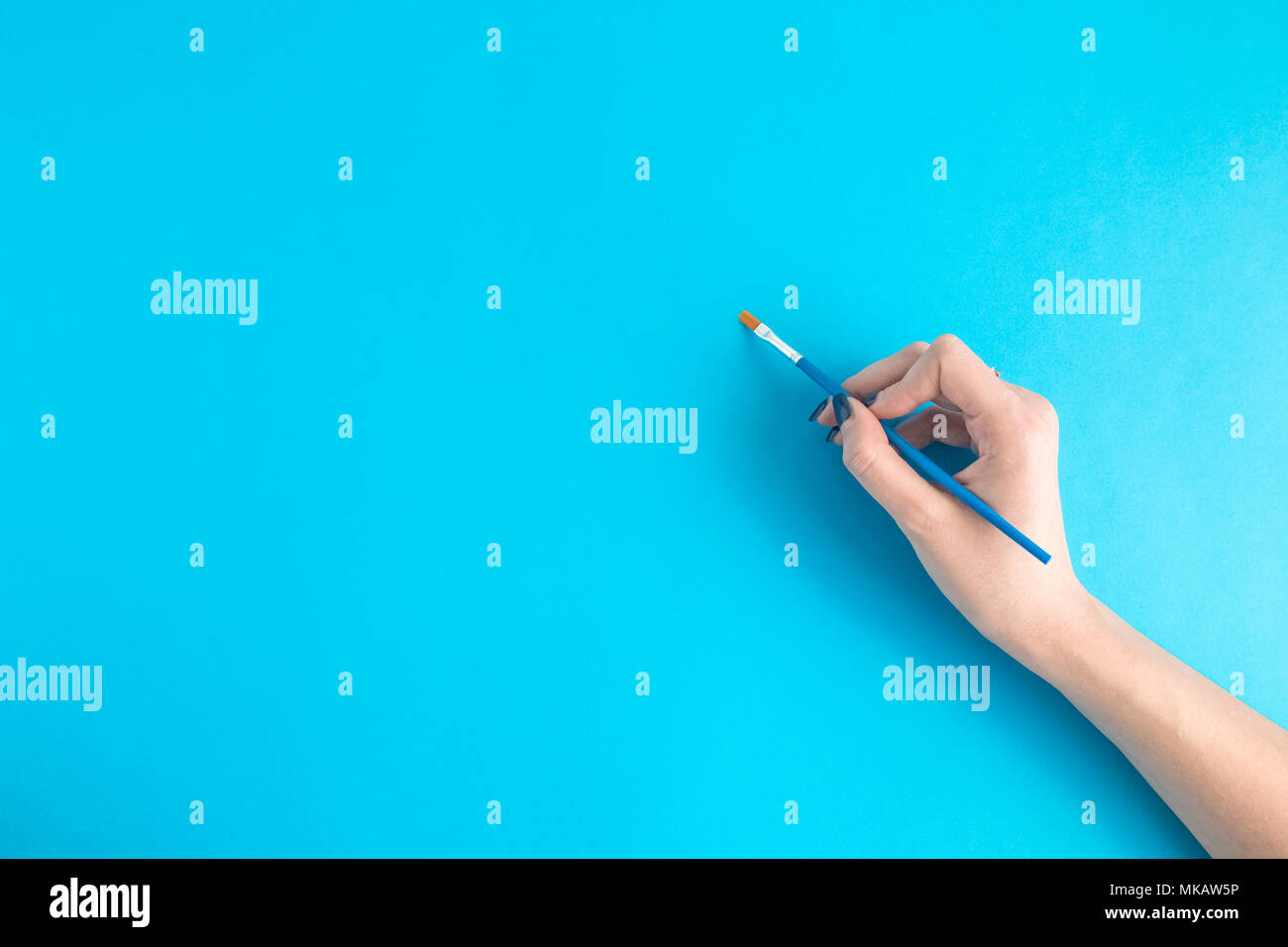 Female hand holding paintbrush against blue background. Space for copy ...