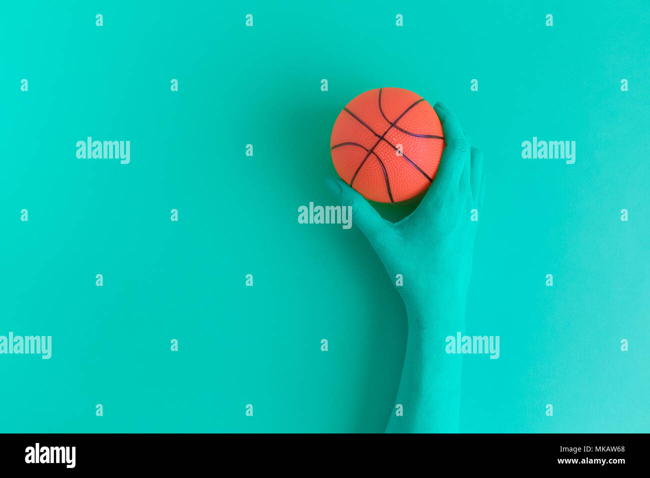 Flat lay of turquoise green colored hand holding small basketball ball minimal creative concept. Space for copy. Stock Photo